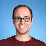 Smiling man wearing a maroon tshirt and glasses. 
