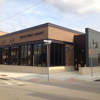 Single-story brown brick library building on a corner in downtown Genoa